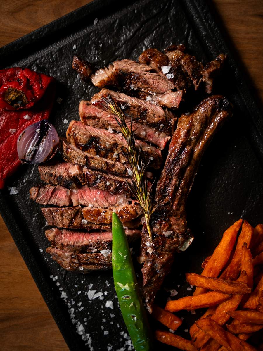 Ribeye Black Angus maturat, feliat pe planșetă, cu ardei copt, ceapă roșie la grătar și cartofi dulci